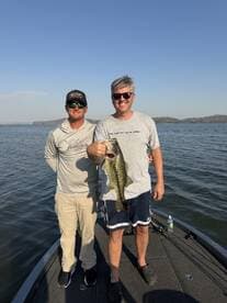 Two anglers proudly displaying a large Largemouth Bass while fishing on a lake.