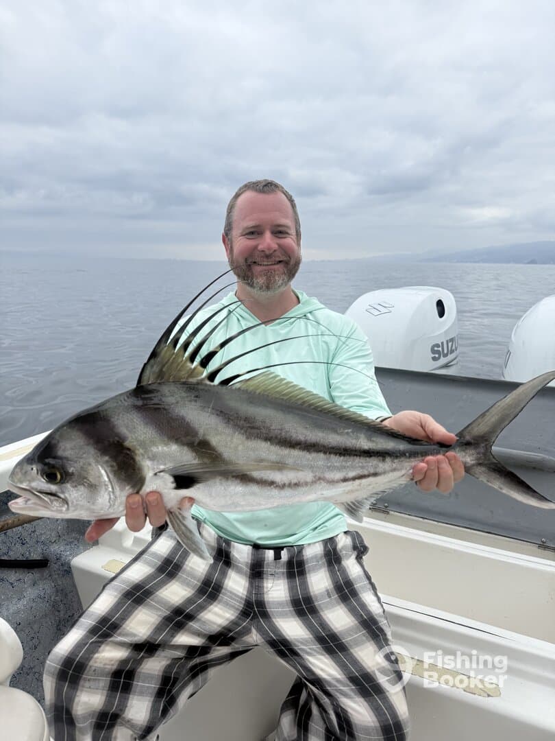 Angler proudly displaying a large Roosterfish while fishing on a boat, showcasing a successful day on the water.