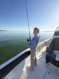 A young angler enjoying a fishing trip on a calm day, casting from the side of a boat.