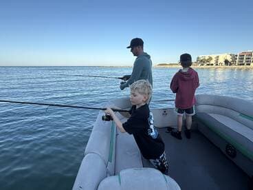 A group of young anglers fishing from a pontoon boat, enjoying a calm day on the water.