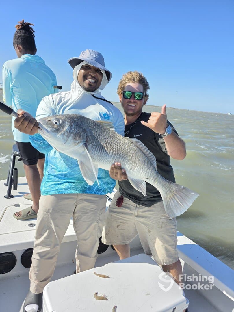 Two anglers proudly displaying a large Redfish on a fishing boat, enjoying a sunny day on the water.