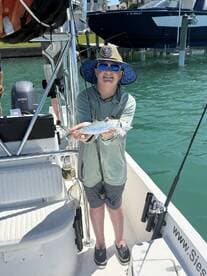 Young angler proudly holding a spotted sea trout while fishing from a boat in a coastal waterway.