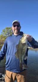 Angler proudly displaying a large Largemouth Bass while fishing on a serene lake.
