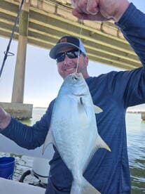 Angler proudly displaying a freshly caught fish under a bridge while fishing from a boat.