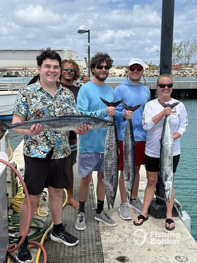 Group of anglers proudly displaying their catch of Barracuda at the dock after a successful fishing trip.