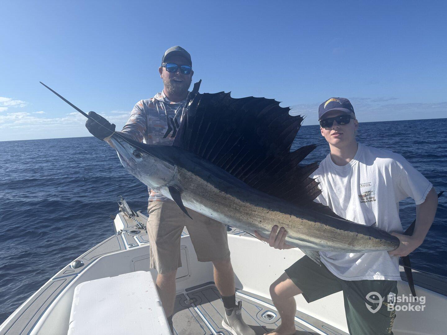 Two anglers proudly displaying a large Sailfish aboard their boat during a deep-sea fishing trip.