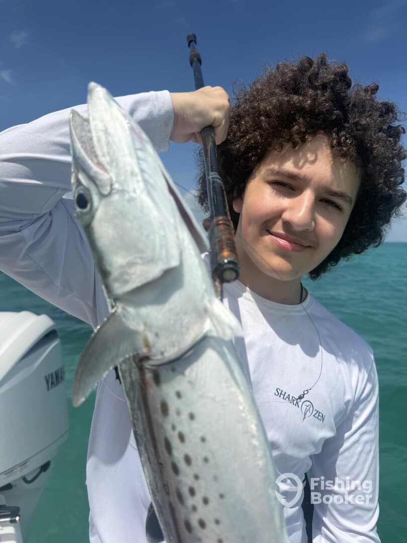 Young angler proudly holding a large fish while fishing on a boat in clear waters.
