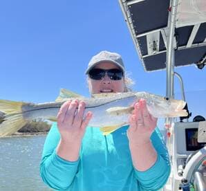 Angler proudly displaying a Snook while on a fishing trip, with a scenic backdrop of water and greenery.
