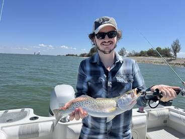 Angler proudly displaying a large Speckled Trout while fishing on a boat in a coastal waterway.