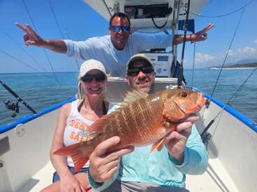 A group of anglers celebrating their catch of a vibrant Snapper while enjoying a sunny day on the water.