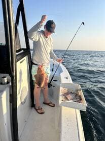 Angler reeling in a Snapper while fishing from a boat in open waters, showcasing an exciting moment on the Gulf Coast.