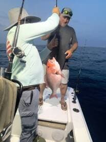 Two anglers celebrating a successful catch of a large Red Snapper while fishing at sea.
