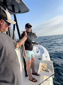 Two anglers on a boat proudly displaying a caught fish, enjoying a sunny day on the water.