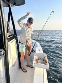 Angler reeling in a large Snapper while fishing from a boat in open waters.