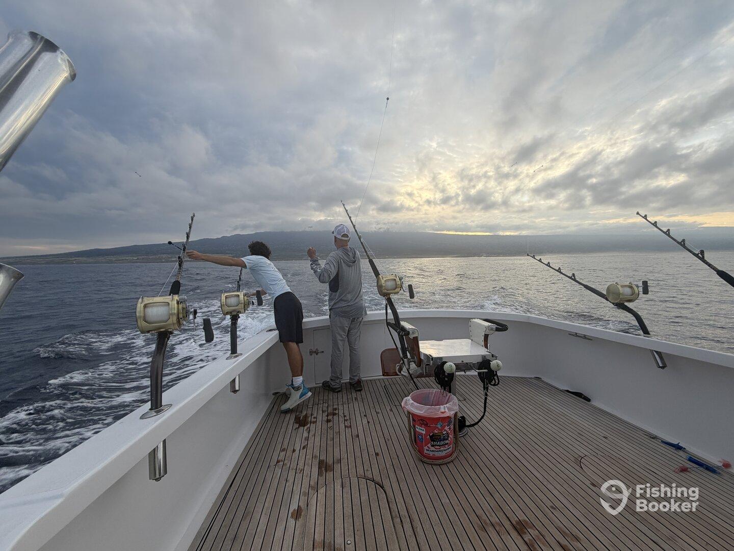 Two anglers actively fishing from a well-equipped boat, casting lines into the open ocean under a dramatic sky.