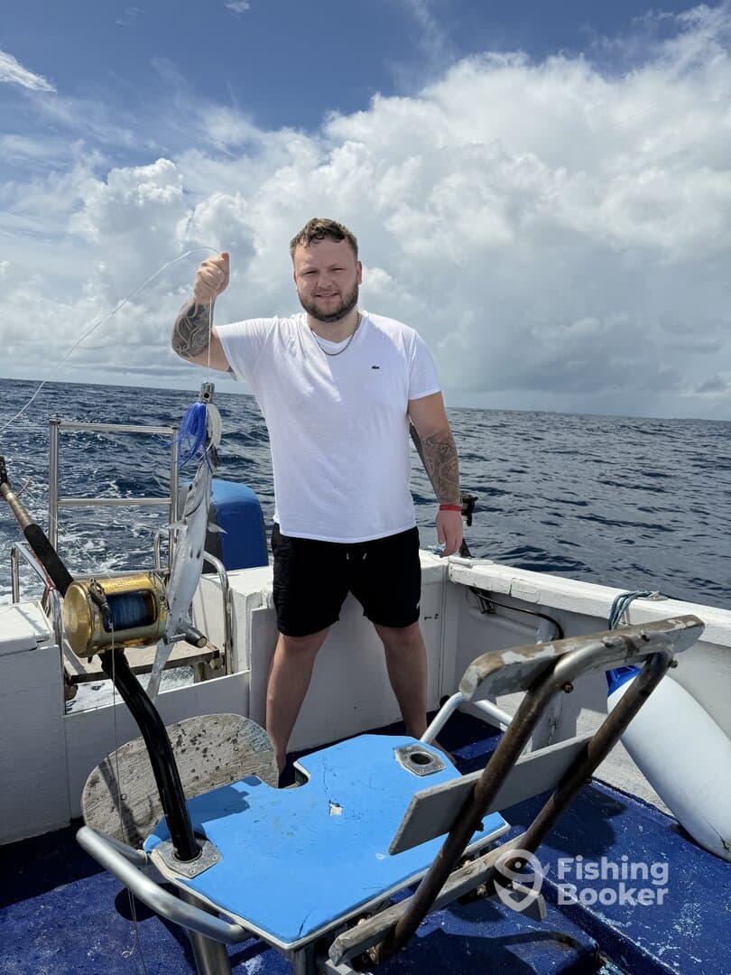 Angler reeling in a catch aboard a fishing boat, surrounded by open water and a clear sky.