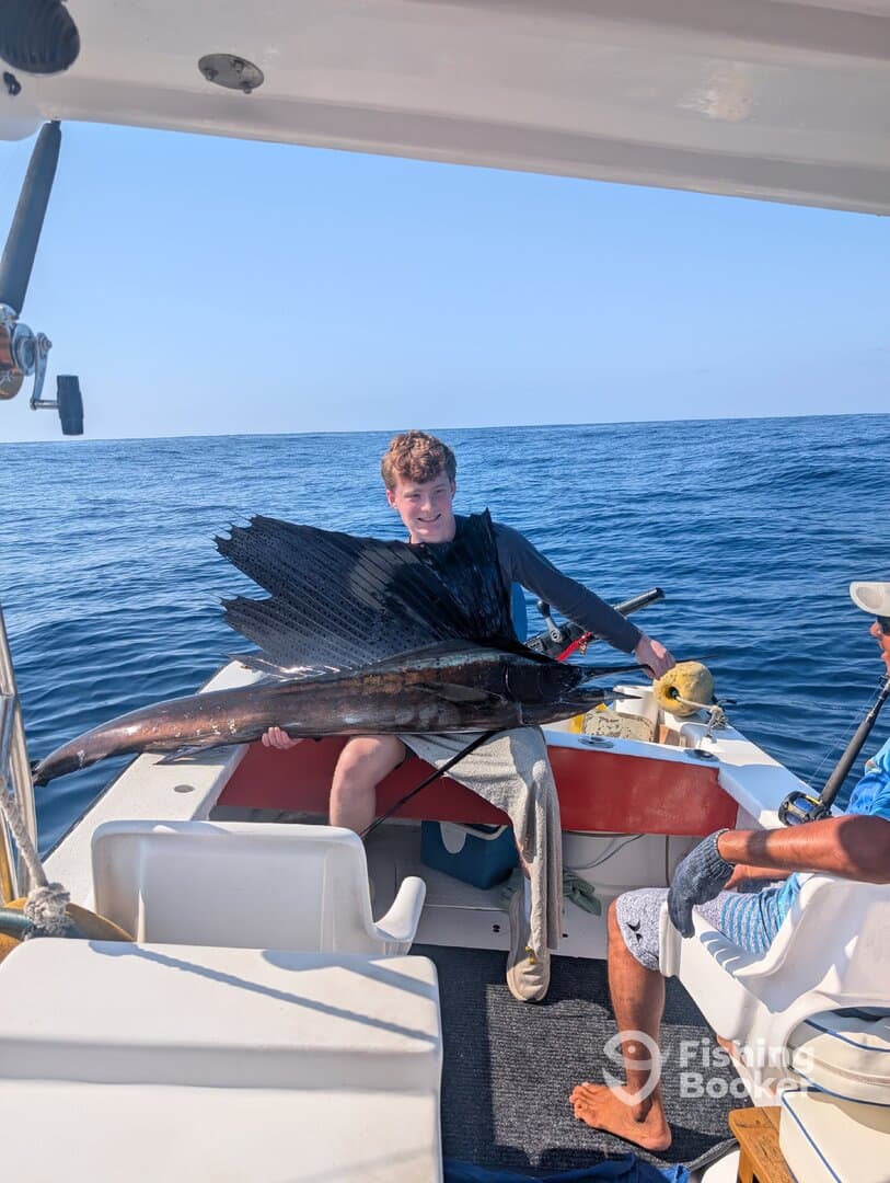 A young angler proudly displays a large Sailfish while aboard a fishing boat in open waters.