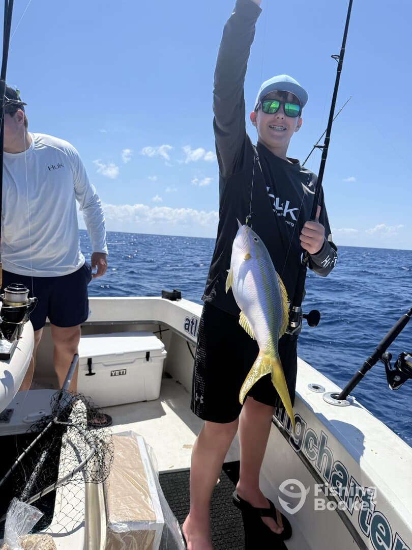 A young angler proudly displaying a colorful fish while fishing on a charter boat in open waters.