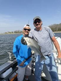 Two anglers proudly displaying a large striped bass while fishing on a boat, enjoying a sunny day on the water.