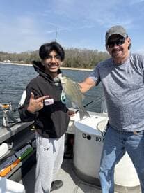 Two anglers proudly displaying a freshly caught Striped Bass while fishing on a boat.