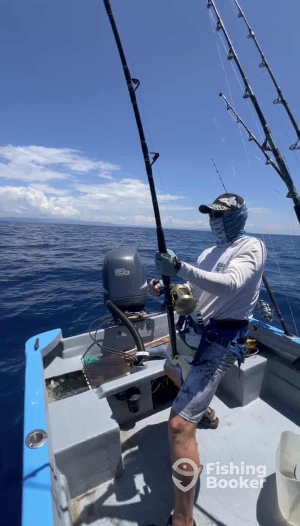 Angler actively reeling in a catch while fishing on a small boat in open water, showcasing a sunny day and calm seas.