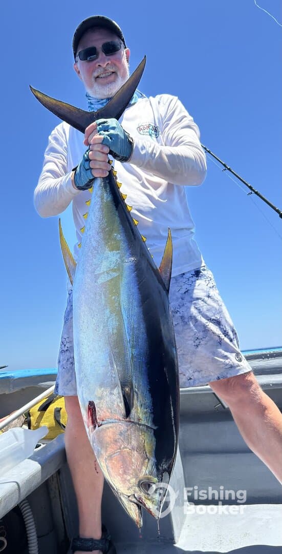 Angler proudly displaying a large Yellowfin Tuna aboard a fishing boat under clear blue skies.