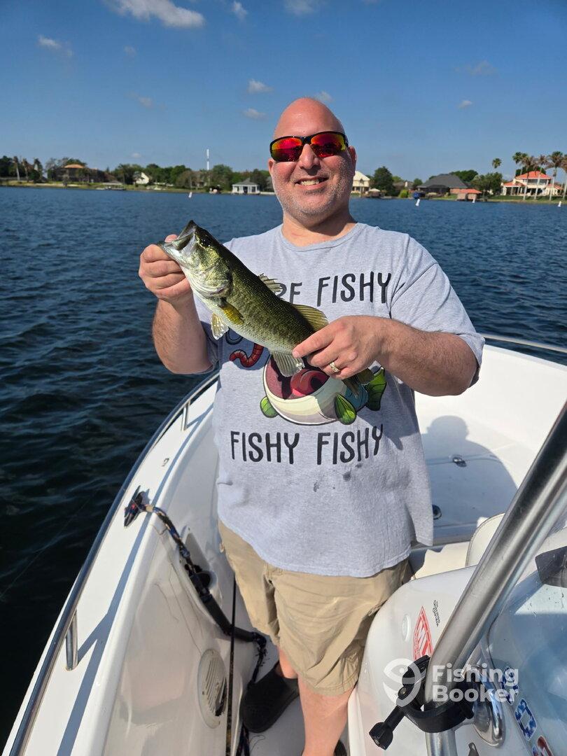 Angler proudly displaying a large Largemouth Bass while fishing from a boat on a sunny day.