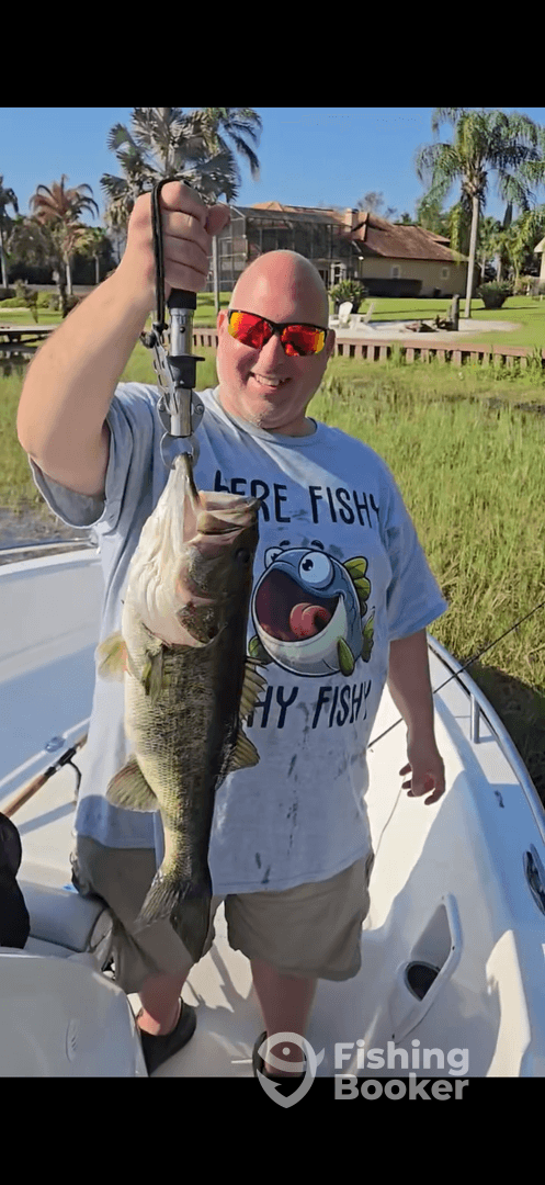 Angler proudly displaying a large Largemouth Bass while fishing from a boat in a scenic waterway.