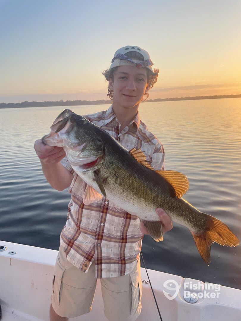 A young angler proudly displaying a large Largemouth Bass during a sunset fishing trip on a serene lake.