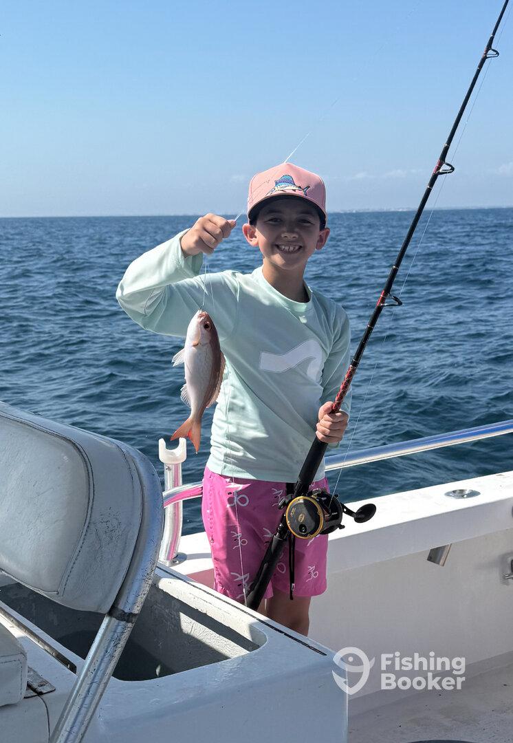 Young angler proudly holding a Snapper while fishing on a boat in open waters.