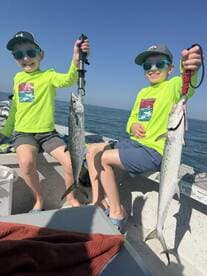 Two young anglers proudly displaying their catches of Spanish Mackerel while enjoying a sunny day on the water.