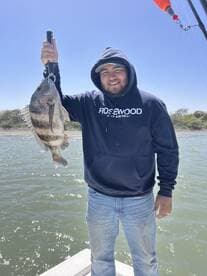 Angler proudly displaying a large Black Drum caught while fishing on a sunny day.
