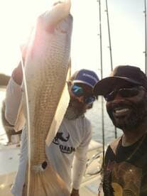 Two anglers proudly displaying a large Redfish while enjoying a day on the water.