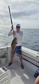 Angler proudly displaying a large Grouper caught while deep-sea fishing on a charter boat.