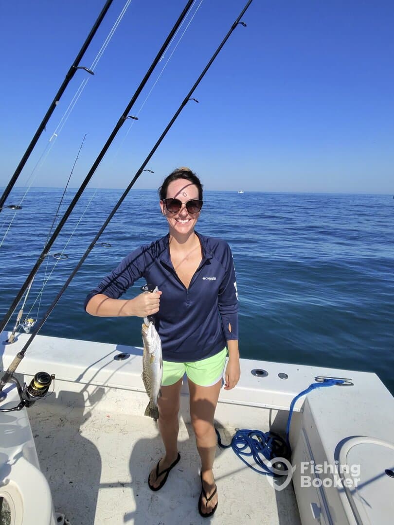 A happy angler holding a freshly caught Speckled Trout while fishing on a sunny day.