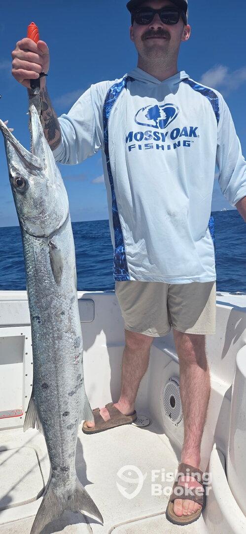 Angler proudly displaying a large Barracuda while fishing offshore, showcasing a sunny day on the water.
