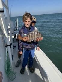 A young angler proudly displaying a large Black Drum while fishing on a boat, enjoying a sunny day on the water.