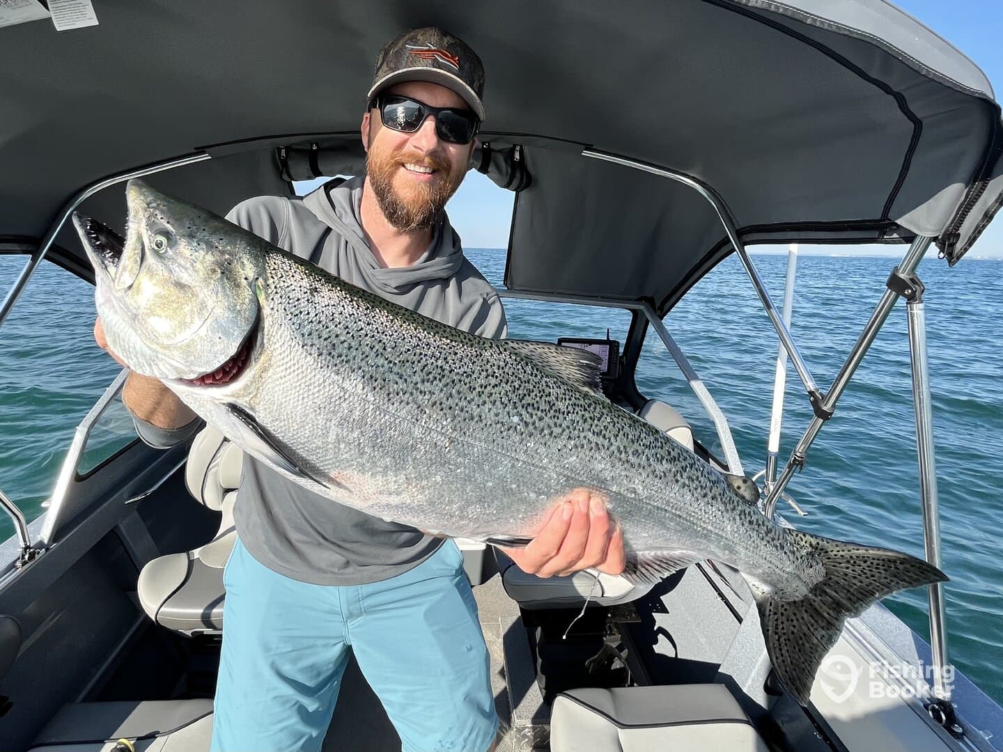 Angler proudly displaying a large Salmon while aboard a fishing boat, showcasing a successful day on the water.