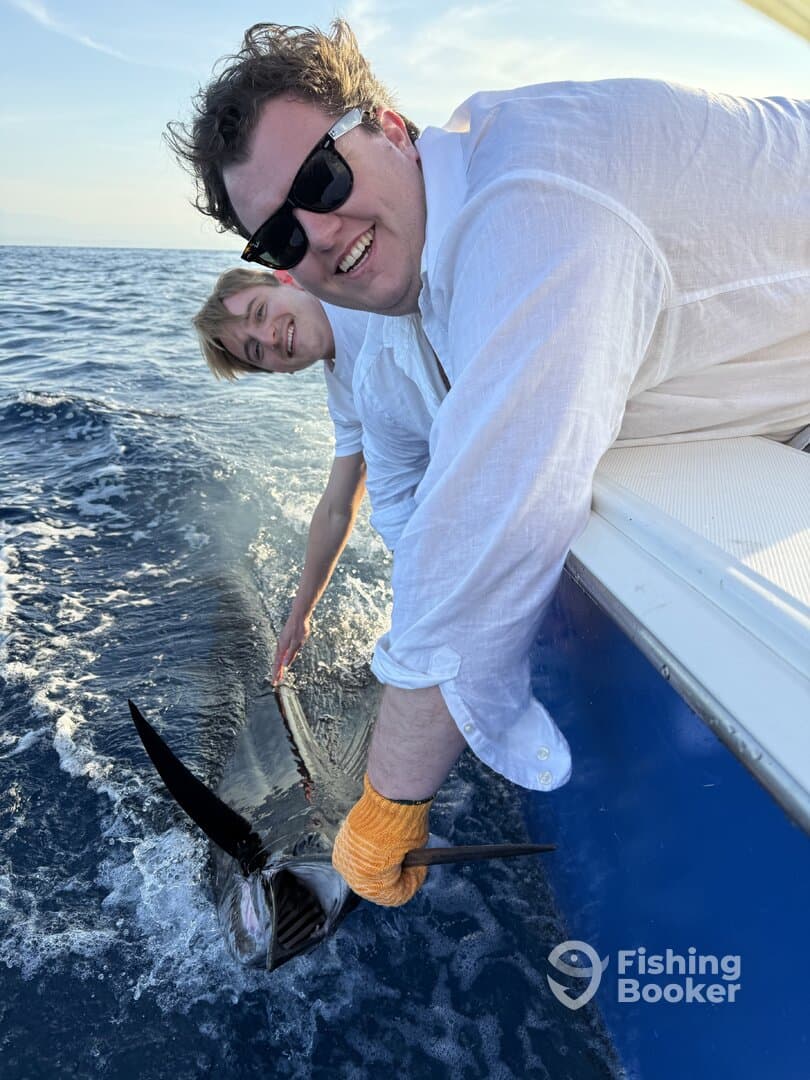 Two anglers actively engaged in reeling in a large fish while enjoying a day on the water.