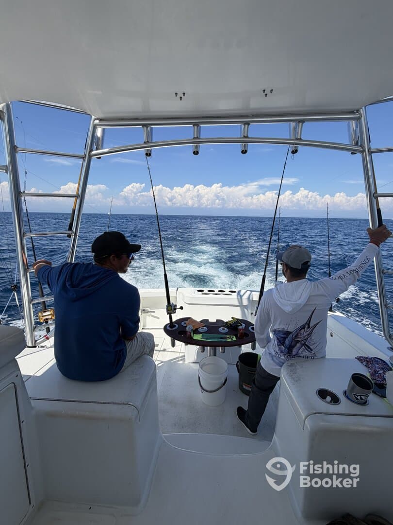 Two anglers seated in the helm area of a sportfishing boat, preparing for a day of deep-sea fishing in clear blue waters.