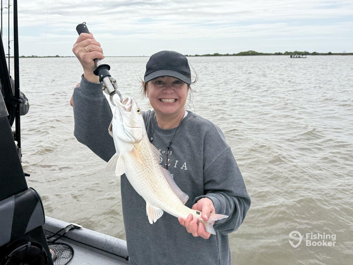 A happy angler proudly displaying a freshly caught Redfish while fishing on a boat in coastal waters.