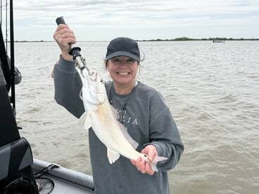 A happy angler proudly displaying a freshly caught Redfish while fishing on a boat in coastal waters.
