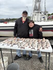 A proud angler and a young boy display their catch of striped bass on a table after a successful fishing trip.
