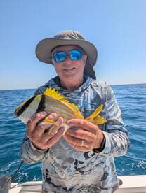 An angler proudly displaying a colorful Yellowtail Snapper while fishing in open waters.