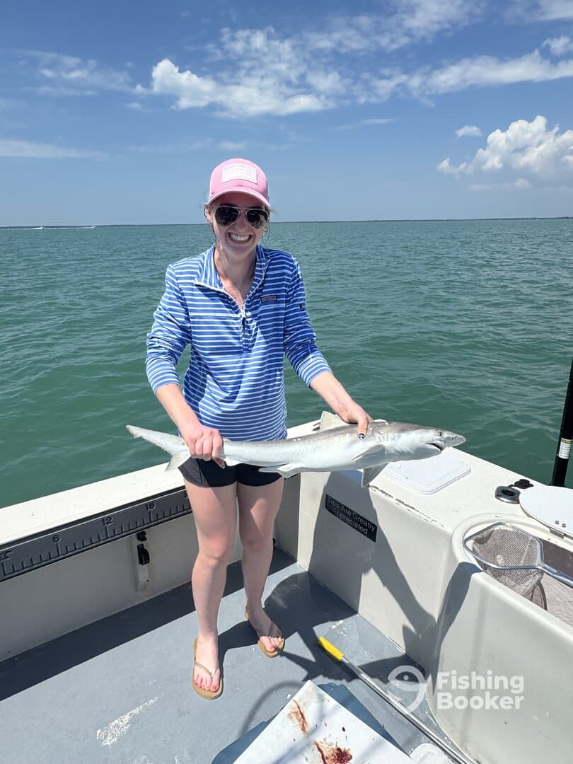 A happy angler proudly displaying a caught shark while fishing on a sunny day.