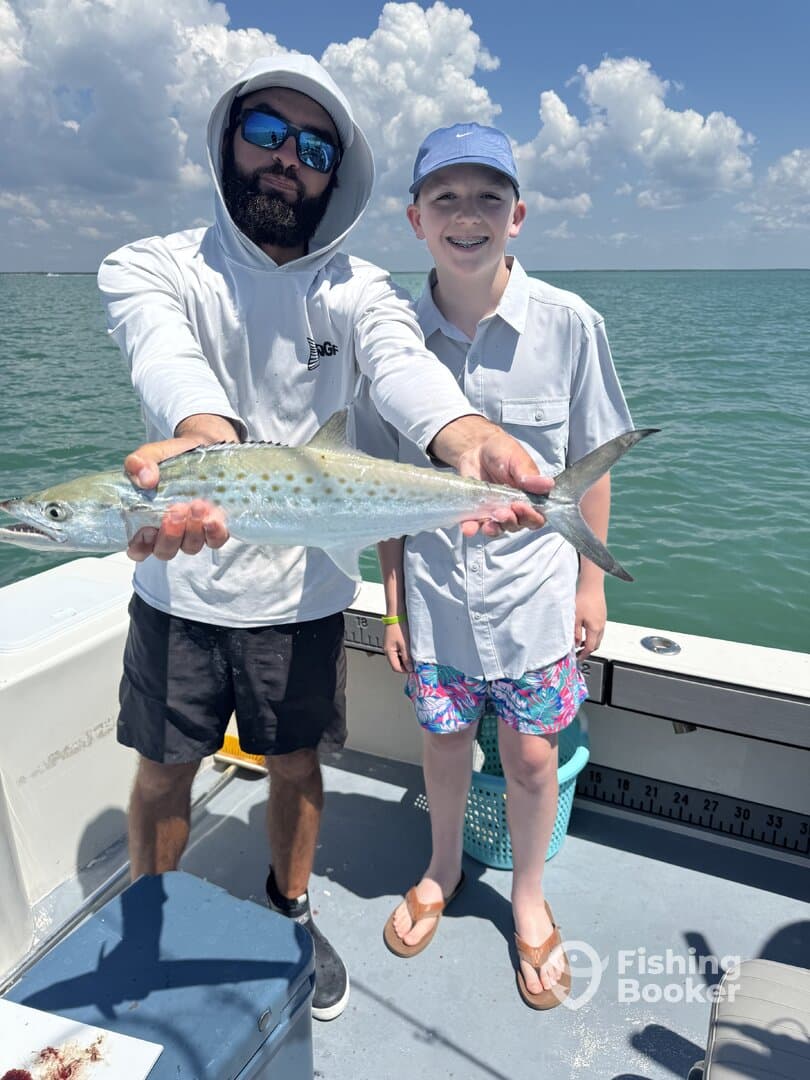 A young angler and an adult proudly display a large Spanish Mackerel while fishing on a sunny day in the Gulf.