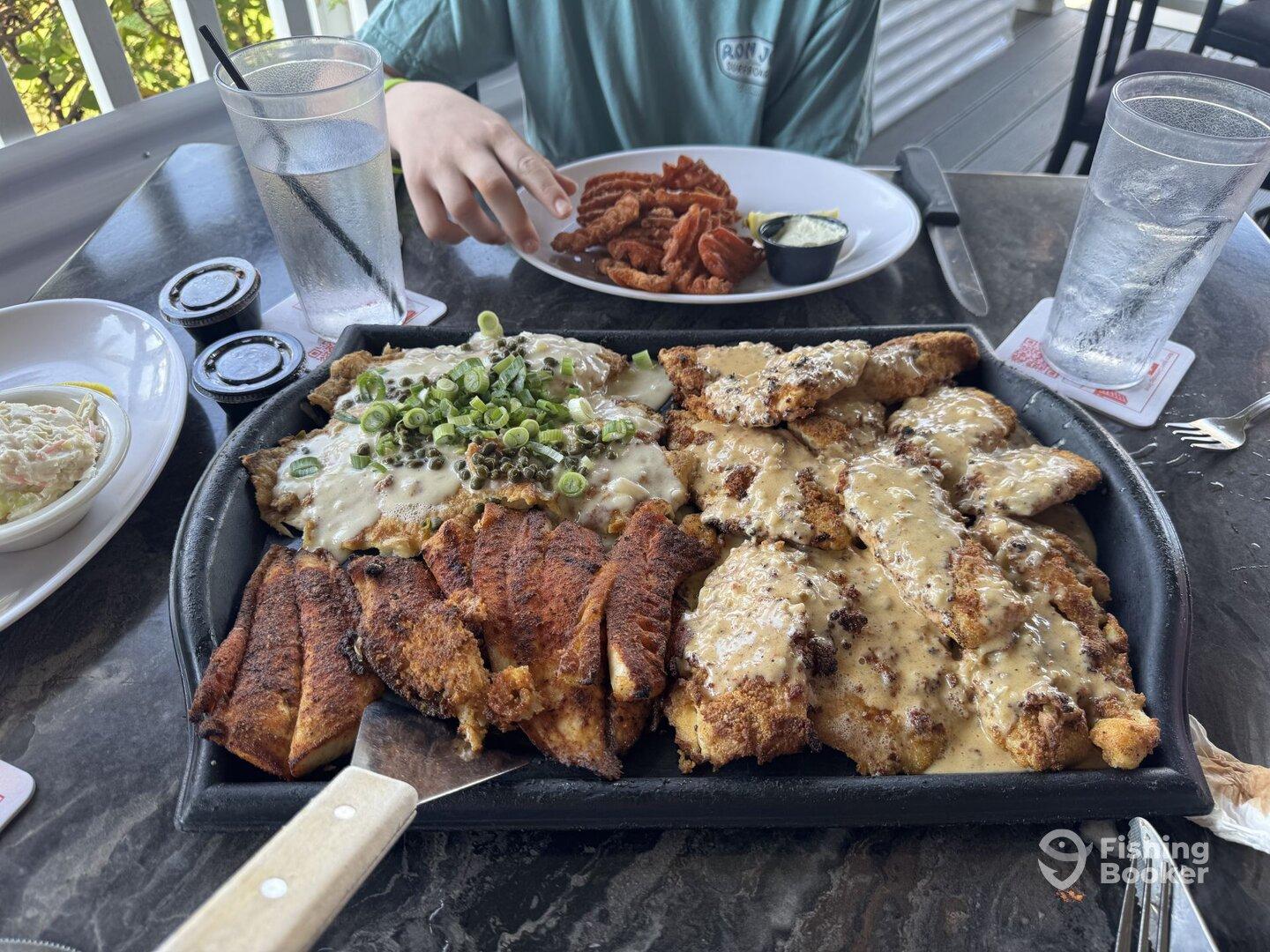 A delicious seafood meal featuring fried fish with toppings, served at a restaurant, with a young person in the background.