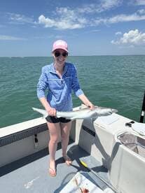 A happy angler proudly displaying a caught shark while fishing on a sunny day.