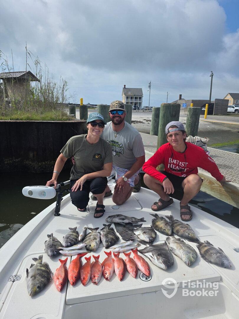 A group of anglers proudly displaying a variety of fish, including Red Snapper and Black Drum, on the deck of a boat after a successful fishing trip.