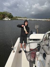 A young angler proudly displaying a Largemouth Bass while fishing from a boat in a calm waterway.